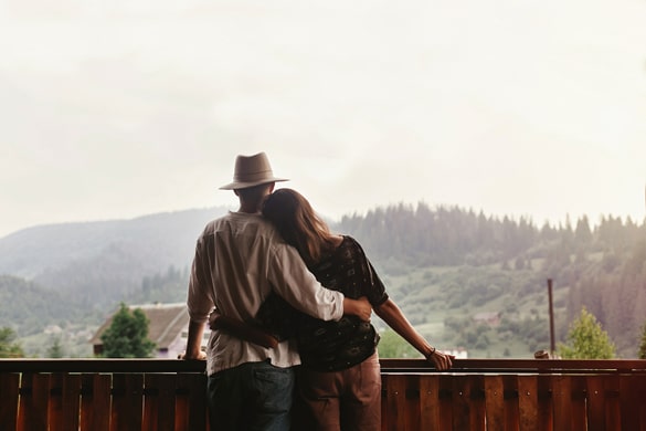 virgo-man-and-virgo-woman-hugging-on-porch-of-wooden-house-looking-at-mountains-in-evening-sunset