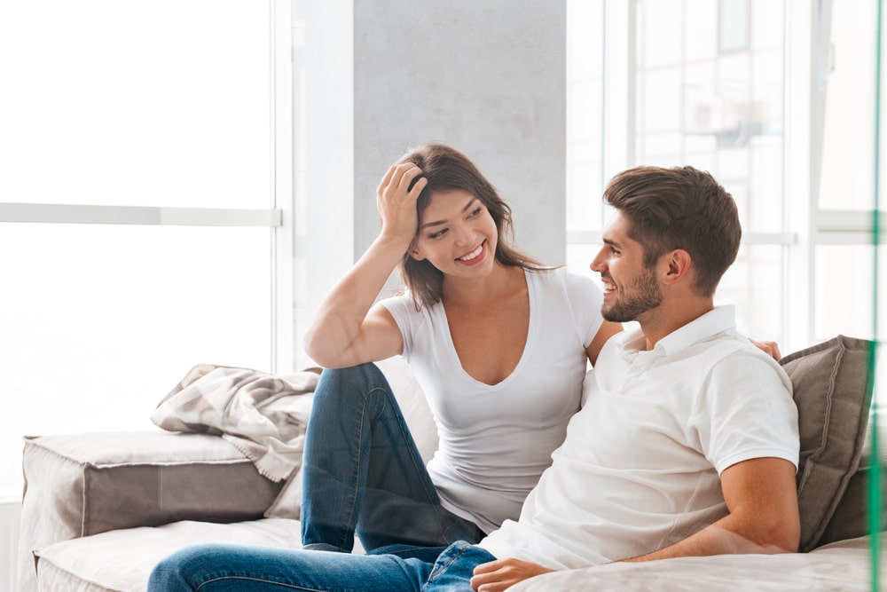 Cheerful beautiful young couple sitting and talking on sofa at home - Virgo...